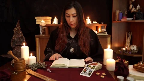 Witch in black mantle hold hands over book, reads magic spell and call spirits. Video stock 108010318