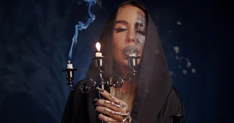 Witch blowing out candle after mystical ritual with blue smoke Stock Footage 320023858
