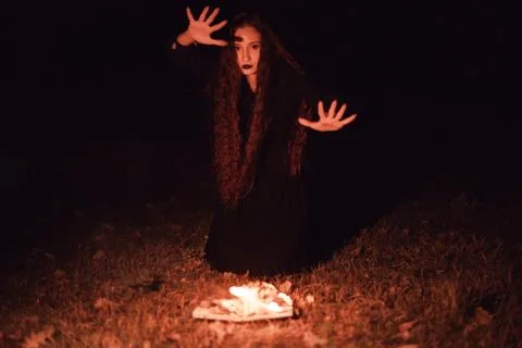 Witch casts a spell over a burning book, mysticism, Halloween, goth woman Stock Photos