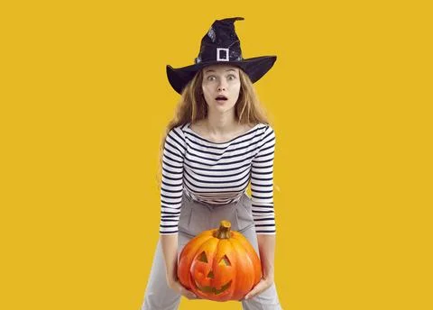 Witch with Halloween pumpkin looking at camera with funny scared surprised face Stock Photos