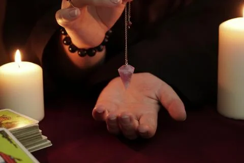 A witch holds amethyst pendulum on chain above hand. Occult and wicca concept. Stock Photos