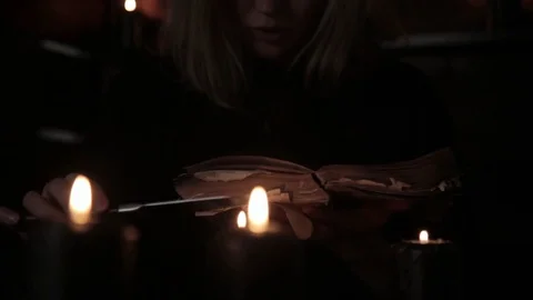 Witch holds a knife and reading spell from old magic book lit by black candles Stock Footage 81614719