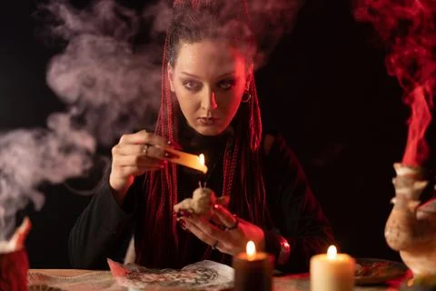 The witch looks straight into the camera and holds a voodoo doll and drips wax Stock Photos