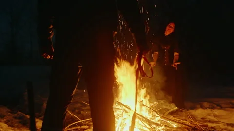 Witch performing witchcraft at bonfire with man standing in foreground Stock Footage 276518192