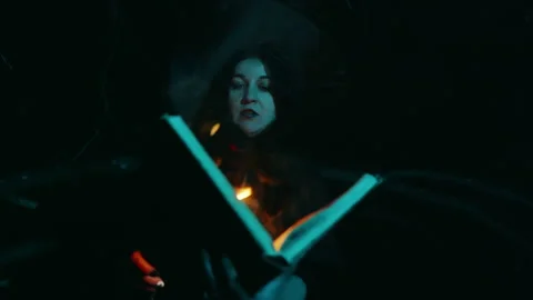 Witch reading magic book with orange light and smoke in dark forest Stock Footage 297653204