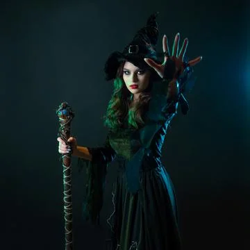 A witch with a staff sends a spell. Young witch in black dress and pointed hat, Foto stock
