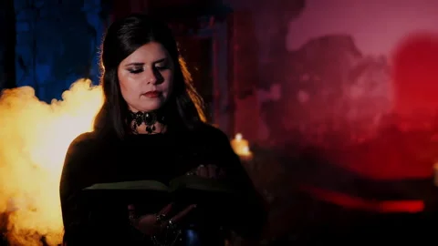 The witch turns over the pages of a magic book and looks into the camera Video stock 285770022