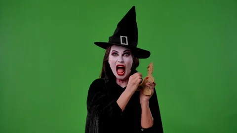 A witch with vampire makeup, wearing a black cloak and hat, poses with a voodoo Stock Footage 316587928