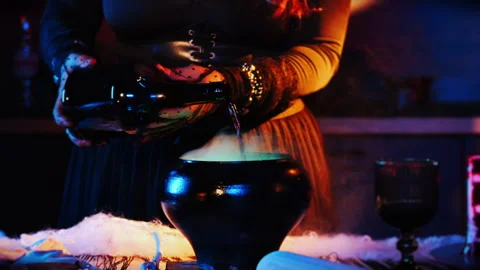 Witch's hands pouring liquid from a black bottle into a magic cauldron. Stock Footage 285369633