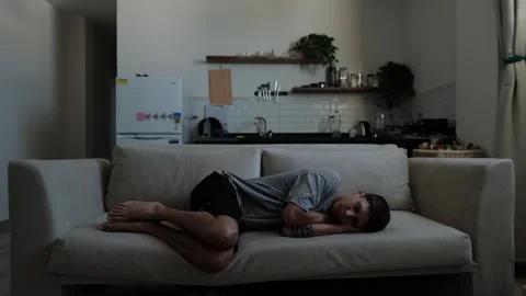Withdrawn man lying alone on sofa feeling emotionally drained Stockbeeldmateriaal 346244117