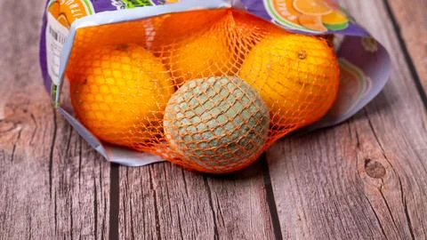 Within a mesh bag containing oranges, there is a single orange that has gone bad Stock Photos