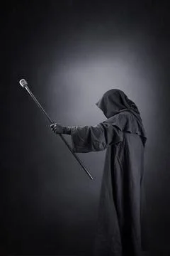Wizard with hooded cape and magic staff over dark background Stock Photos