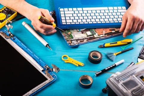 Wizard repairs laptop with tools and hands on the blue wooding table. top vie Stock Photos