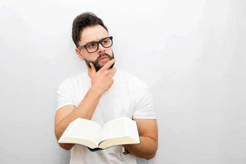 Wize and thoughtful young man in glasses stand and hold opened book in hands. He Photos
