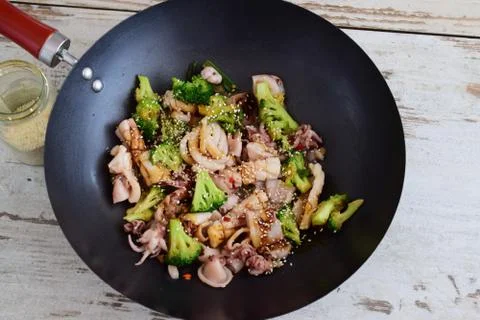 Wok fried squid with broccoli, soy sauce and sesame seeds. Stock Photos