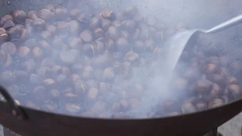 A wok full of chestnuts is tossed over an open flame, releasing a warm, nutty Stock-Footage 307378304