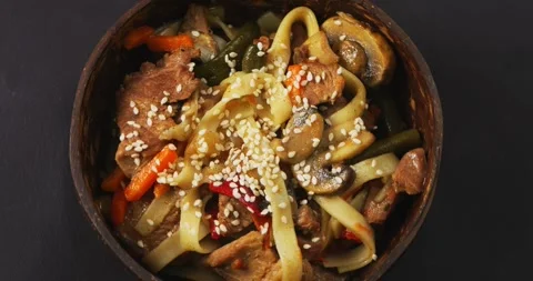 Wok udon with beef in a coconut shell plate sprinkled with sesame seeds in sauce Stock Footage 256459206