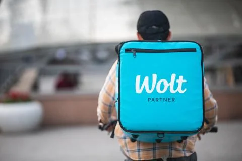 WOLT logo on a blue box by a courier on a bicycle - international food delivery Stock Photos