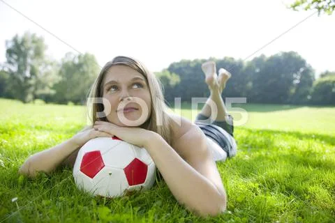 Woman (20-25) lying in field, leaning on football, close-up Stock Photos