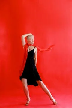 Woman 40 45 years old in a black dress dancing tango on a red background Stock Photos