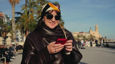 The woman actively uses the device during her walks: browsing social media Stock Footage 334944149