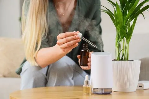 Woman adding essential oil to diffuser for aromatherapy and wellness, home co Stock Photos