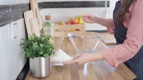 Woman adding flour to a bowl to make pizza dough in her home kitchen Stock Footage 128201925
