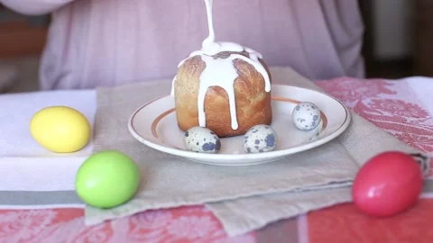 Woman adding glaze on the top of the Easter cake. Colored eggs on a table Stock Footage 114291185
