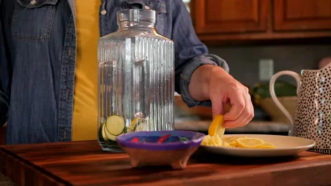 Woman adding lemon to glass container for flavored water. Video stock 138333091