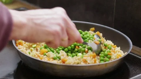 Woman adding peas to a pan with fried rice with carrots and spring onions Stock Footage 84493970