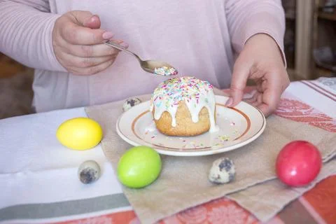 Woman adding sprinkles on the top of the Easter cake. Colored eggs on a table Stock Photos