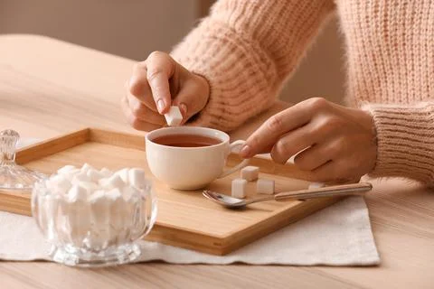Woman adding sugar cube to a cup of hot tea on a wooden tray, sweetening beve Stock Photos