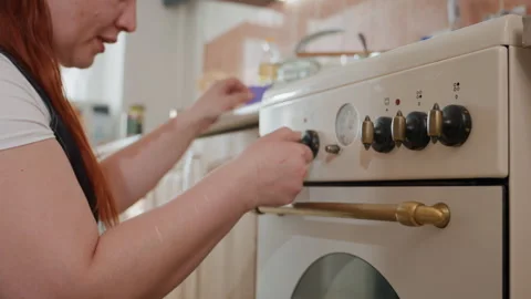 Woman adjusting black control knobs on cream enamel stove in cozy home kitchen Stock-Footage 343677756