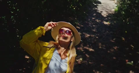 Woman Adjusting Hat on Forest Path in Sunshine Vídeo Stock 323887730