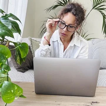 Woman adjusting her spectacles while looking intently at a laptop screen, w.. Stock Photos