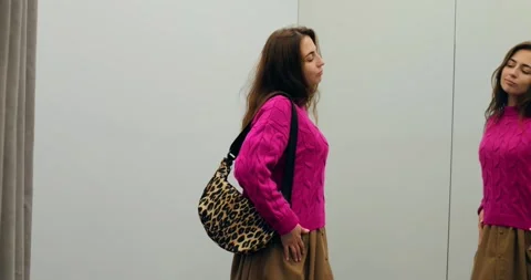 Woman adjusting leopard bag in fitting room mirror, bag pattern showcased with Stock Footage 314467746