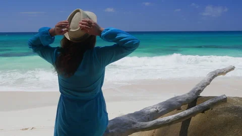 Woman adjusting straw hat on beach with ocean waves background Stock Footage 346367413