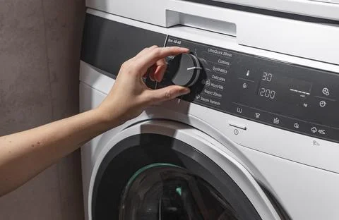 Woman adjusting washing machine program selector dial. Adult female operating Foto stock