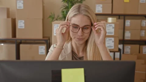 Woman adjusts glasses at computer while checking parcel labels with stacked.. Video stock 337361144