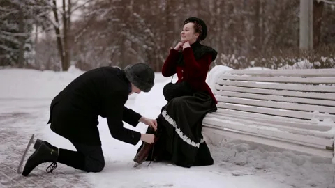 A woman adjusts her hat while a man carefully ties her shoe.  Stock Footage 301299446