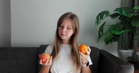 Woman analyzing two oranges on couch, fresh fruit selection, organic Stock Footage 305934783