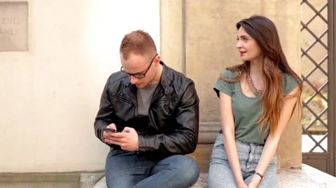 Woman and man sitting on the street. He is focused on his phone. (48) Stock Footage