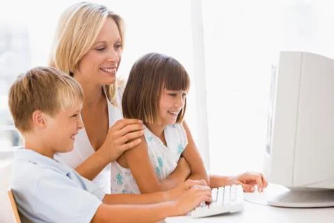 Woman and two young children in home office with computer smiling Stock Photos