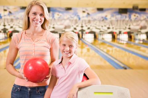 Woman and young girl in bowling alley holding ball and smiling Stock Photos