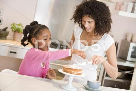 Woman and young girl in kitchen icing a cake smiling Stock-Fotos