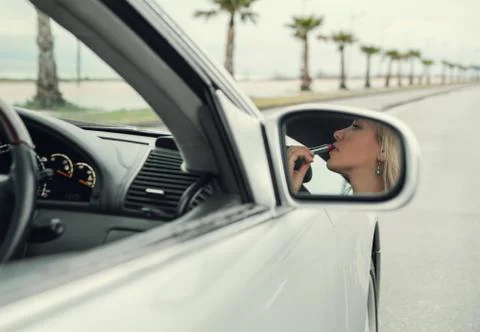 Woman apply  lipstick looking in rear view car mirror Foto stock