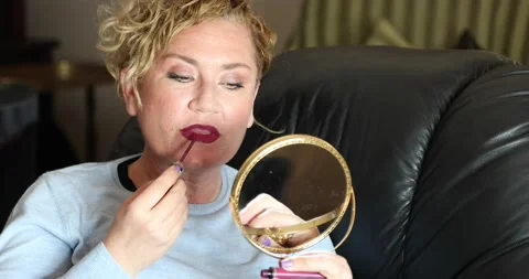 Woman applying lipstick while doing makeup on sofa at home 2 Stock Footage 150245015