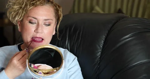 Woman applying lipstick while doing makeup on sofa at home Stock Footage 150245026