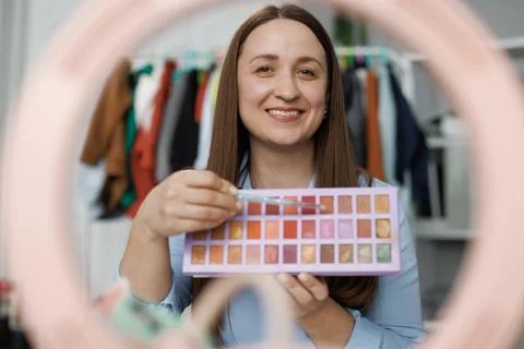 Woman applying makeup on face with brush while recording vlog for social media Stock Photos