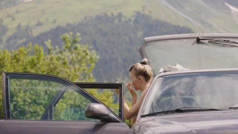 Woman applying makeup while sitting in car on scenic mountain road Stock Footage 301402495